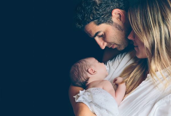 Happy couple embracing and looking newborn over dark background